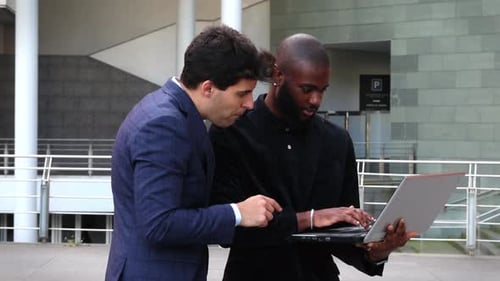 Multicultural businessmen reviewing company data on laptop in financial district