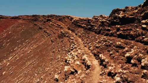 Woman Hiker Walking on Cliff Edge Overlooking Volcano with Big Barren Brown Land of Crater