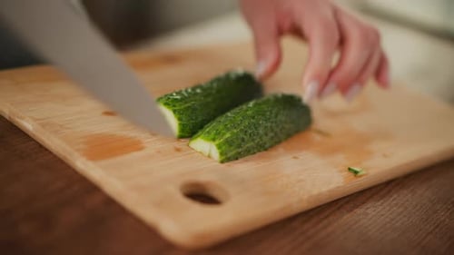Close Up of Person Slicing Cucumber Into Two Parts on Cutting Board