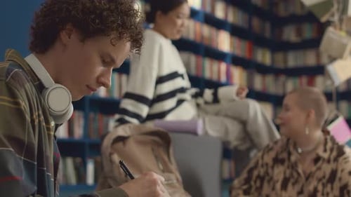 Estudiante varón caucásico escribiendo en un cuaderno en la biblioteca