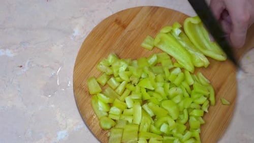 Fresh green bell pepper slices being prepared on rustic wooden board with hands