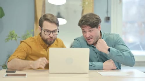 Two Men Celebrate Success at Laptop in Office