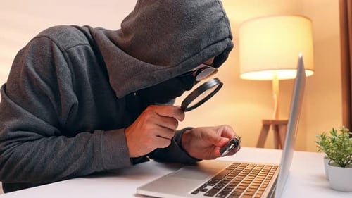 A hacker inspects a combination lock with a magnifying glass.