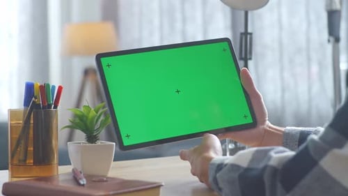 Close up of man's hand using a mock up green screen tablet on a desk