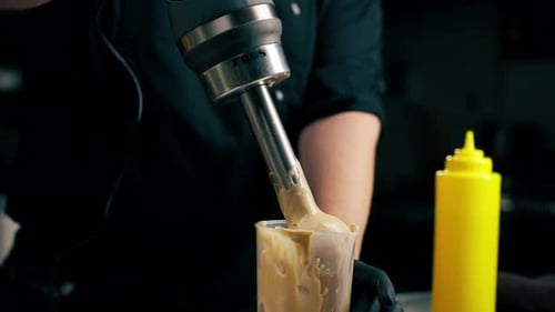 in a Professional Kitchen a Chef Prepares a Sauce for Salad Beats It with a Mixer Adding Ingredients