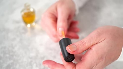 Hand Applying Yellow Cuticle Oil to Fingernails