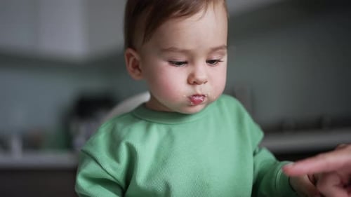 Um lindo bebezinho com comida na boca está sentado na mesa de alimentação.
