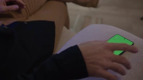 Man Sitting On Sofa Gets Cellphone With Green Screen. closeup shot