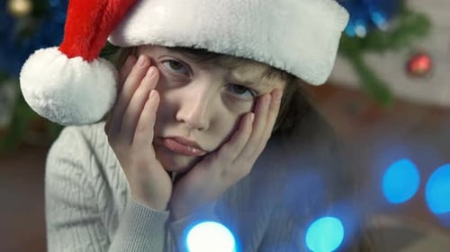 Sad Child Wearing Santa Hat by Christmas Tree