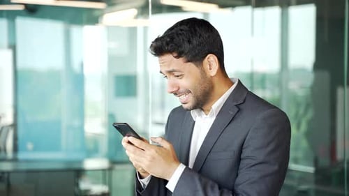 Side view. Happy young businessman in a formal suit received great news on smartphone while standing