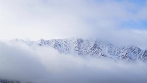 Clouds moving over the with snow covered mountain peaks while the sun is shining
