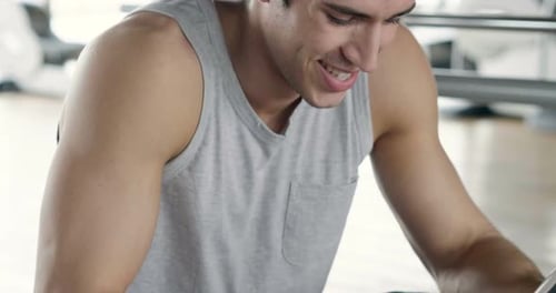 Portrait of a guy in a gym while resting between a workout and the other uses his phone to watch s