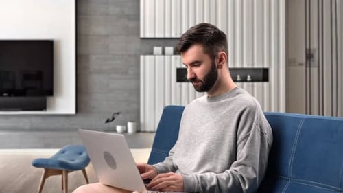 Modern Man Working Remotely Laptop Browsing Internet Analyzing Information Sitting Couch Home Office