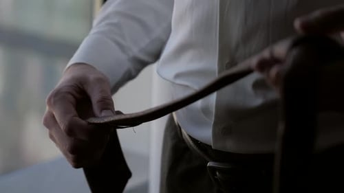 Closeup of a Man at the Window in a White Shirt Holding a Tie in His Hands