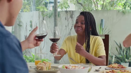 Multi-ethnic Couple Clinking Glasses while Sitting at Table with Their Friends