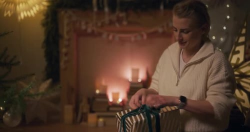Woman Tying Christmas Gift Ribbon Near Fireplace