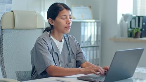 Female Physician Working on Laptop at Desk in Clinic