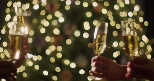 Un groupe de personnes boit des verres de vin mousseux sur fond de sapin de Noël flou
