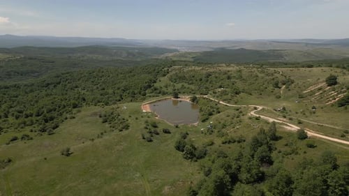 Luftaufnahme einer friedlichen ländlichen Landschaft mit einem kleinen Teich, unbefestigten Straßen und üppigem Grün