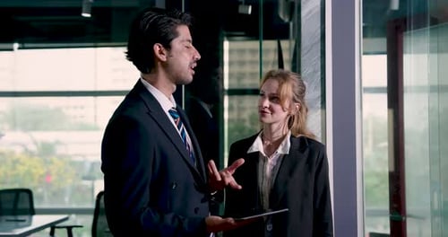 Businessman presenting idea to businesswoman using digital tablet during relaxed office meeting.