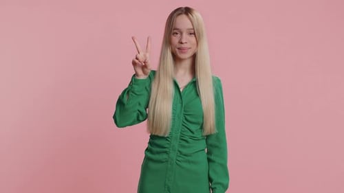 Smiling Woman Making Peace Sign Against Pink Background