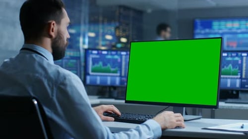 Stock Market Trader Working on a Computer with Isolated Mock-up Green Screen. In the Background Mon
