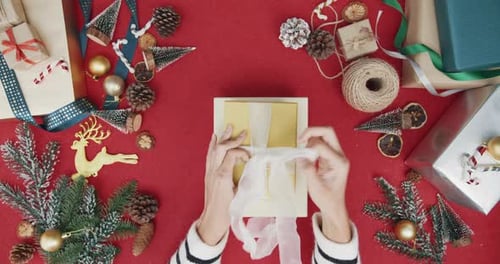 Top view of girl hands unpacking present gift box winter christmas decorations on red background.