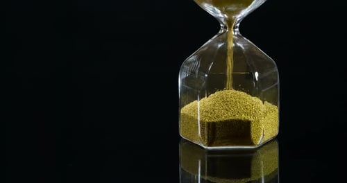 Golden Grains Flowing in Hourglass on Black