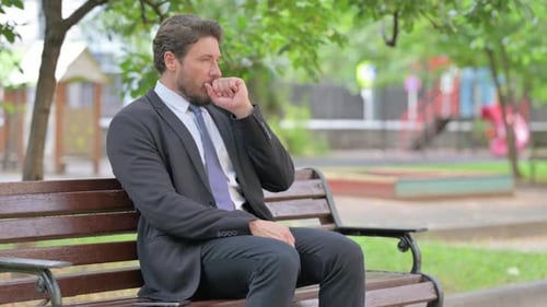 Man Coughing While Sitting on Park Bench Outdoors