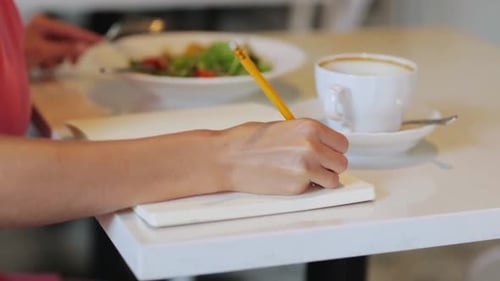 Woman Eating Salad and Writing in Notebook