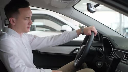Young Business Man Stroking the Steering Wheel in an Electric Car Buying a New Car at a Dealership