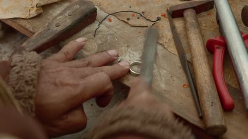 Handwerker arbeitet an einem Silberring und feilt Schmuckstück mit Werkzeugen auf einem Holztisch ab, Tay Nguyen.
Vietnam