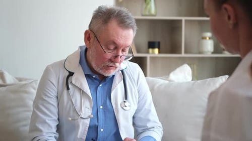 Senior Man Doctor Examining Yound Woman in Doctor Office or at Home Girl Patient and Doctor Have