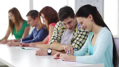 Education, Friendship And School Concept - Five Smiling Students Writing In Textbooks And Sitting...