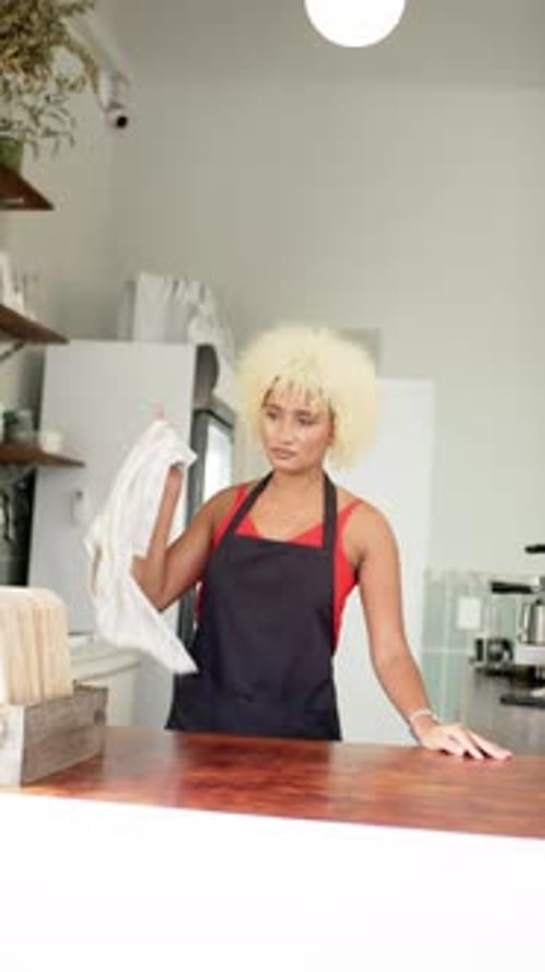 Vertical video: African American female barista cleaning counter in modern cafe, wearing apron