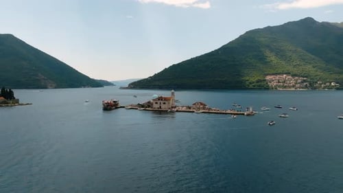 Cinematic aerial drone view of Our Lady of the Rocks island with its stone church, tourists, and sur