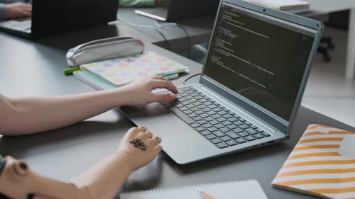 Close-up of Unrecognizable Girl with Prosthetic Arm Typing Code on Laptop