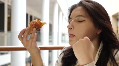 L29. A girl tastes a crispy croissant in a shopping center.