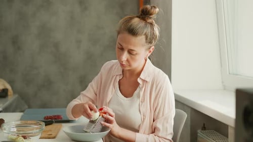Female Chef Grating Cheese Into Bowl In Bright Kitchen Setting