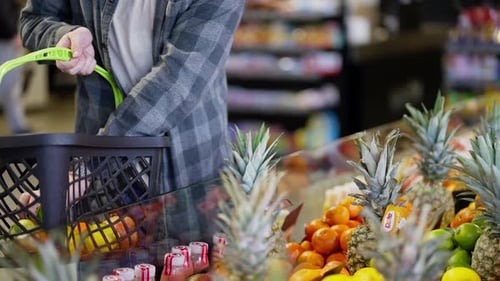Close Up a Supermarket Customer in a Plaid Shirt Selects the Fruit He Needs Among the Orange Mango