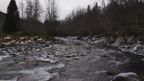 River with a strong current flowing through the woods, with stones in the middle and ice and snow