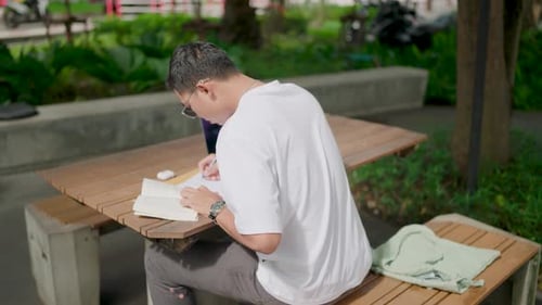 Man studying and writing while working outdoors in a park during a summer day.