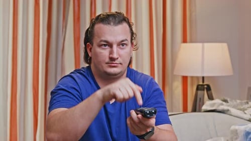 Man using remote control while sitting on sofa indoors