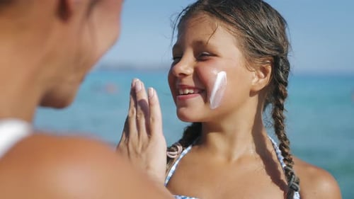 Nahaufnahme einer jungen Mutter, die schützende Sonnencreme oder Sonnencreme auf ihr kleines Happy S aufträgt