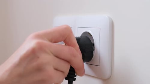 Une main insère une prise Euro dans une prise Euro accrochée au mur