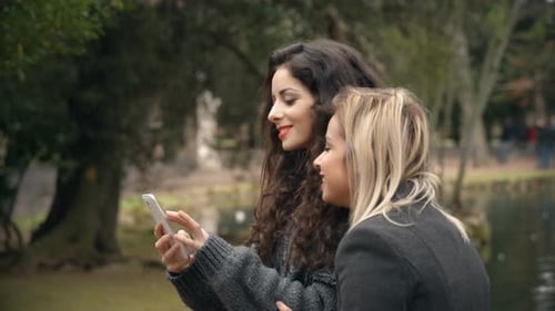 two girlfriends have fun at the park watching photos on the smartphone