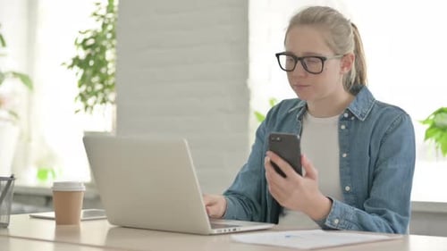 Beautiful Young Woman Using Smartphone While Using Laptop in Office
