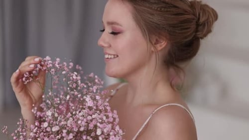 Smiling Woman Holding Pink Flowers in Indoor Setting