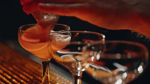 Bartender Strains Orange Cocktail into Stemmed Glass at Bar