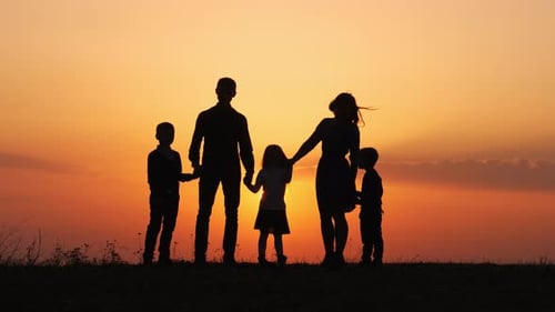 Silhouettes of Happy Family Holding the Hands in the Meadow During Sunset